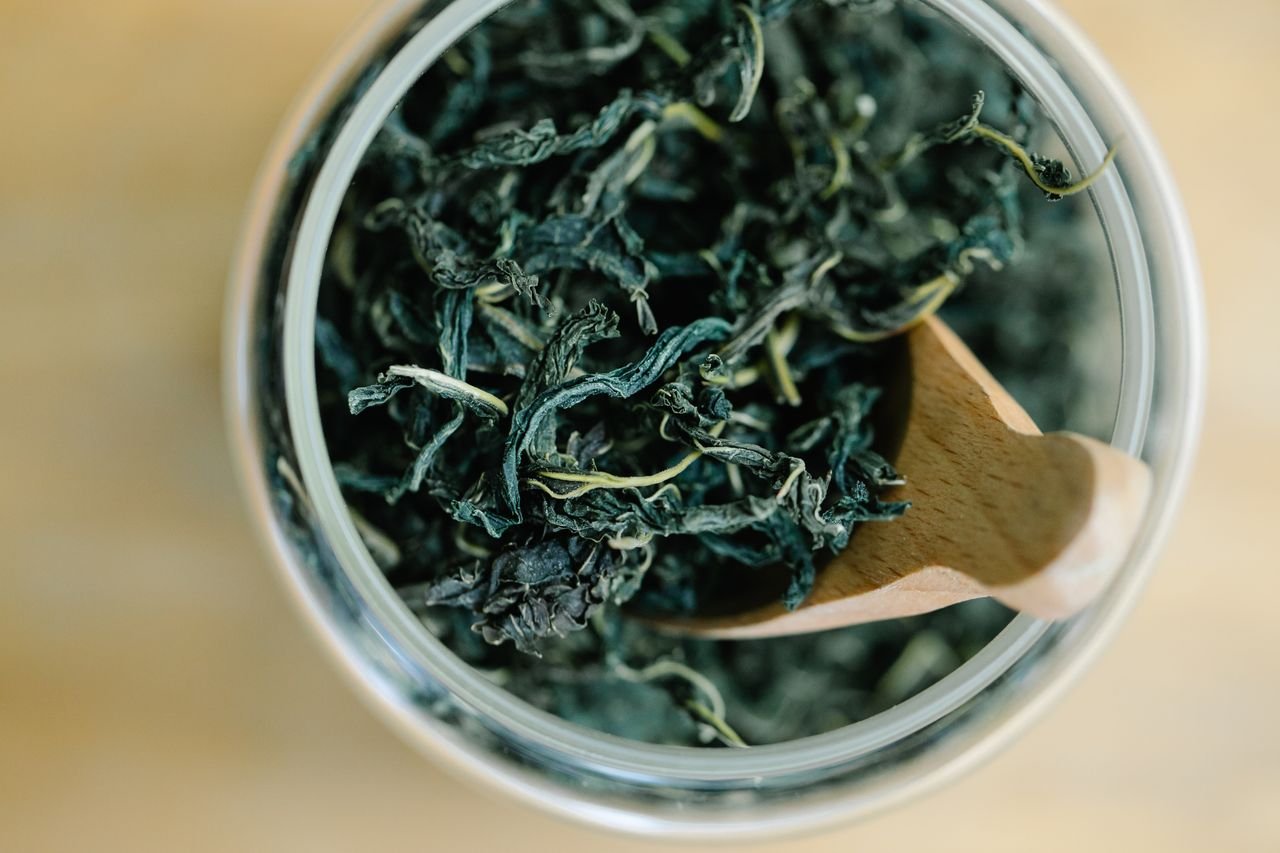 Crafting Captivating Headlines: Your awesome post title goes here Top view of dried green tea leaves in a glass jar with a wooden spoon.